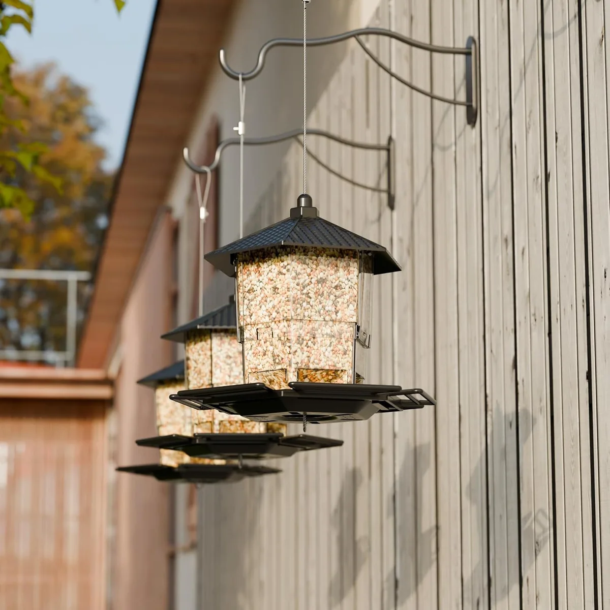 Black hopper bird feeders hanging from wall hooks in a sunny backyard setting
